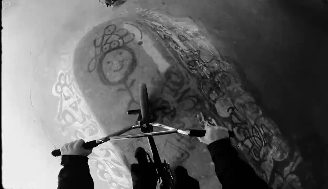 Vista en primera persona de un ciclista recorriendo un bowl cubierto de grafiti, en blanco y negro
